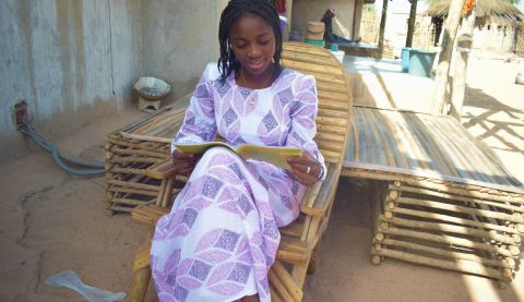 A girl reading a text book while sat on a chair outdoors