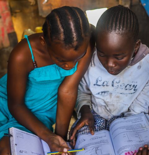 Two girls writing in a copybook with their heads down