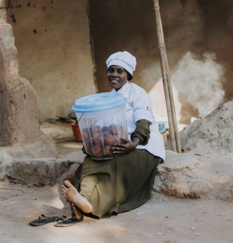 A woman holding a bucket of food in her lap and smiling