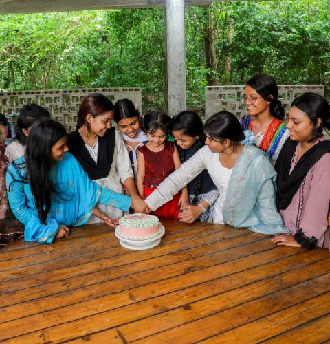 Girls sat around a table and cutting a cake in Bangladesh