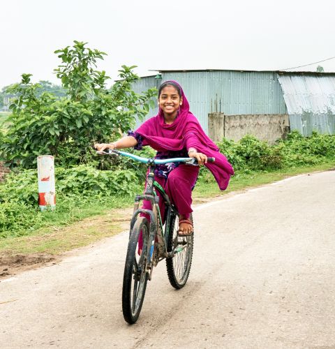 Girl on her bike smiling happily in Bangladesh.