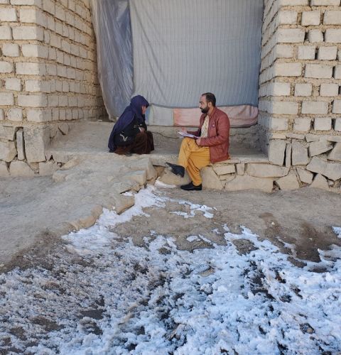 A woman sits on the ground with snow around, speaking to a man in Afghanistan