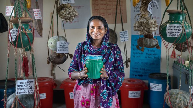 A woman in a purple scarf holding a vase or a pot and smiling