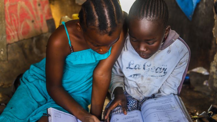 Two girls writing in a copybook with their heads down