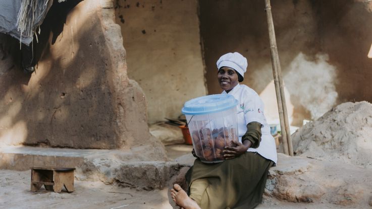 A woman holding a bucket of food in her lap and smiling